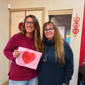 woman holding heart card standing with another woman