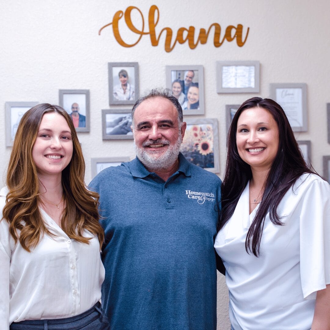 two women and man standing in front of a wall of photos.